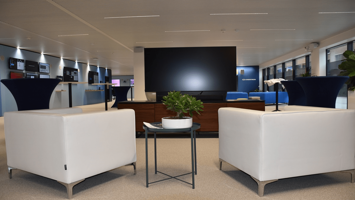 Modern lounge area at the Crestron Experience Center Mechelen featuring white seating, a large display screen, and minimalist interior design