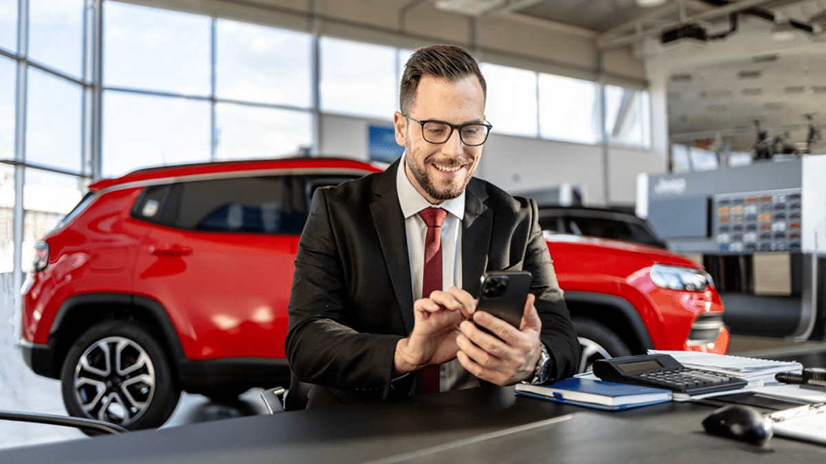 An employee using GoTo Connect’s AI Receptionist in a car showroom with a red car behind him