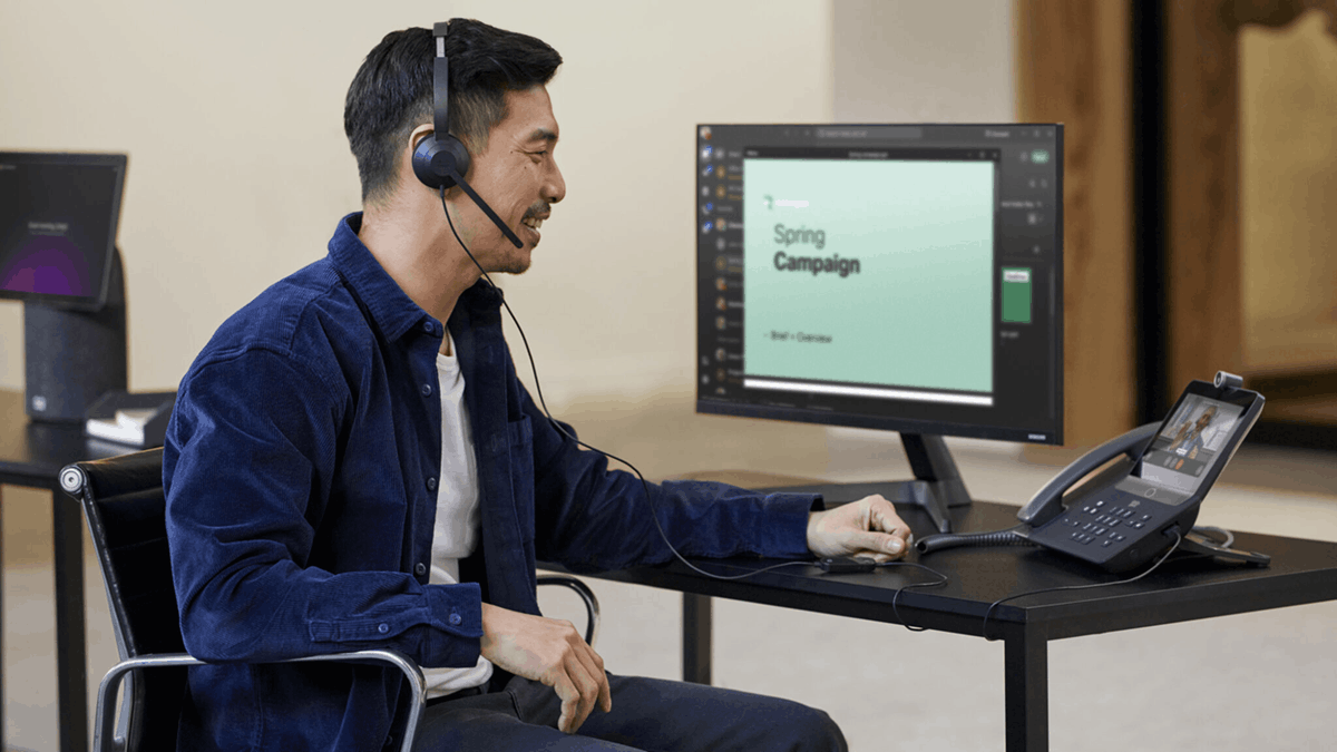 Office worker using a headset while managing a call on a desk phone and computer setup
