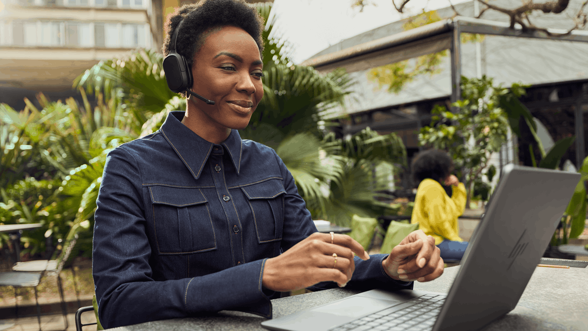 Professional using an HP Poly Focus 6 Bluetooth headset while working remotely on a laptop in an outdoor setting