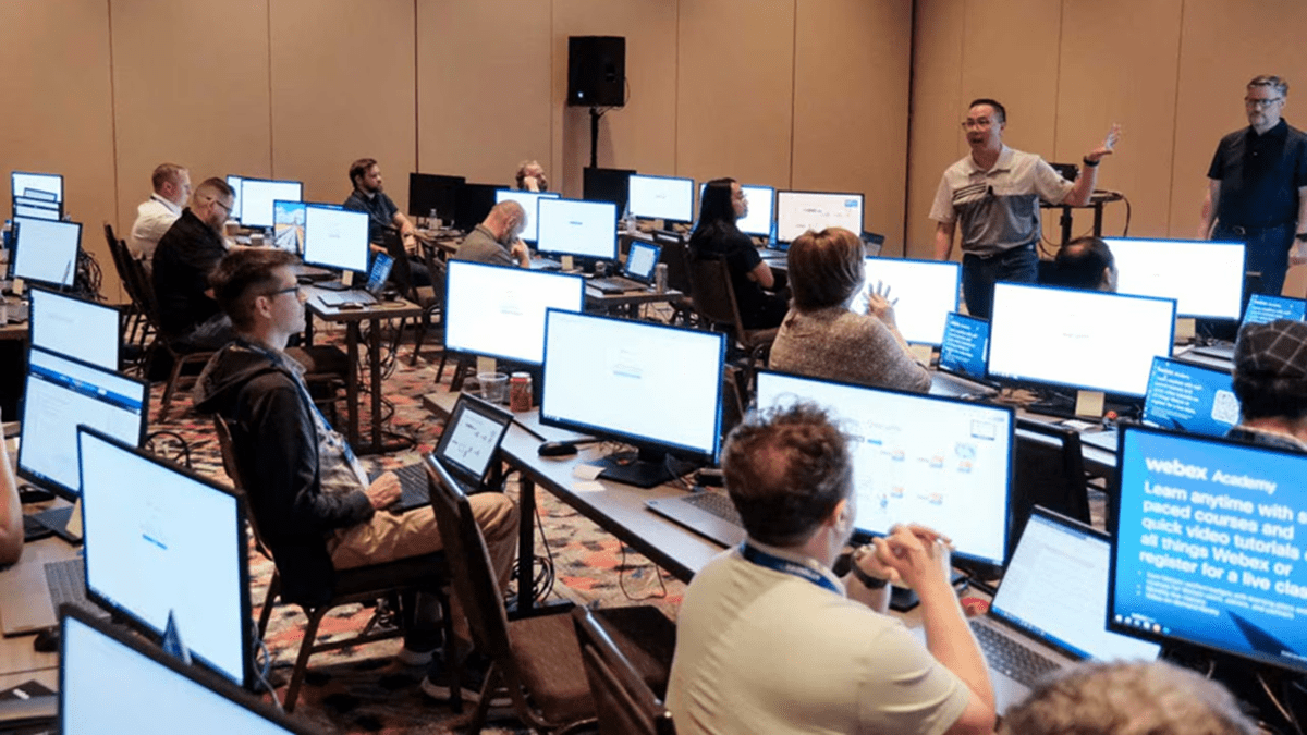Conference room with attendees at computer stations listening to a speaker
