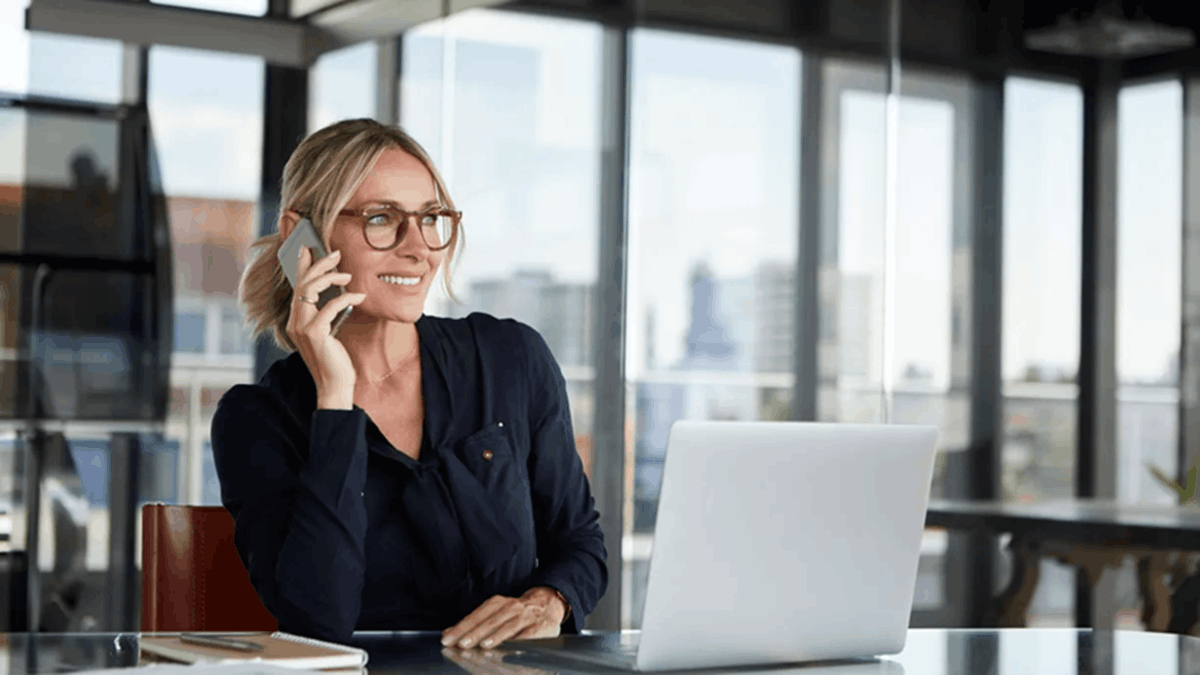 Woman talking on a smartphone while working on a laptop in an office
