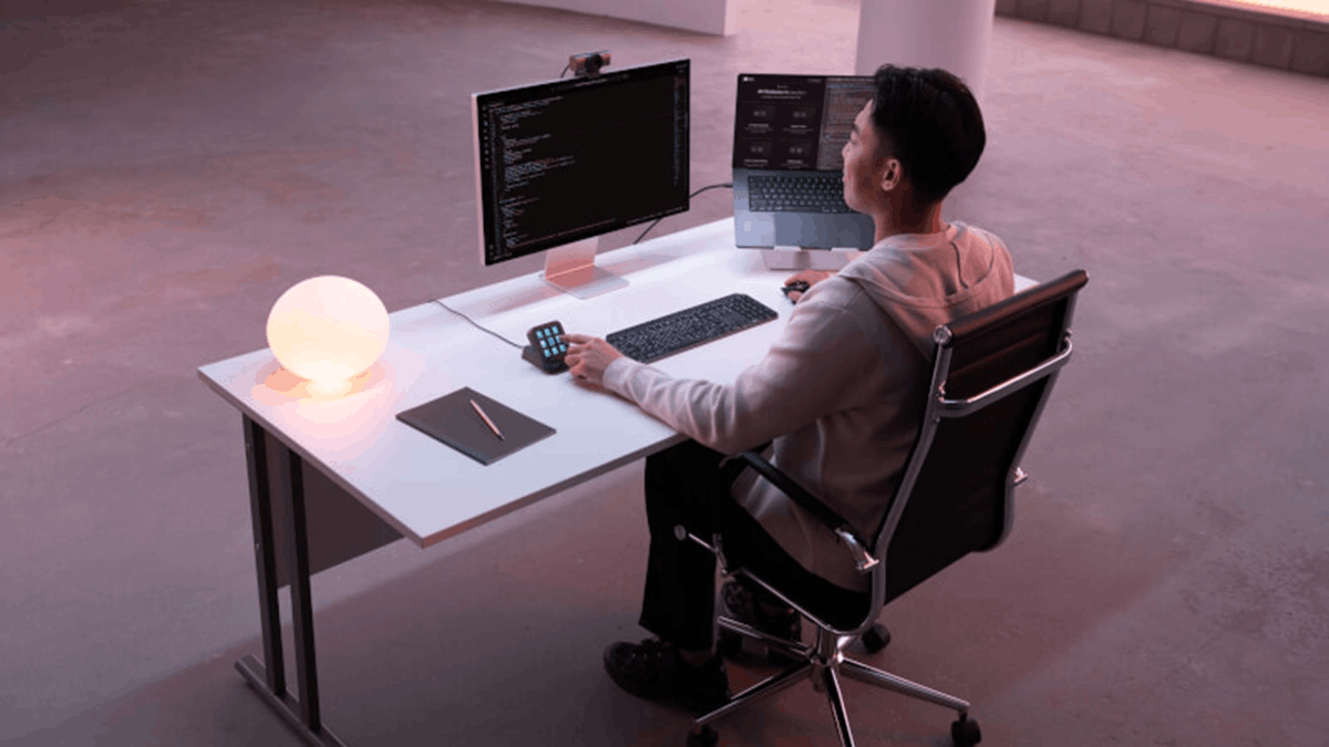 Developer working at a multi-monitor desk while using the Logitech MX Keypad alongside a keyboard and laptop