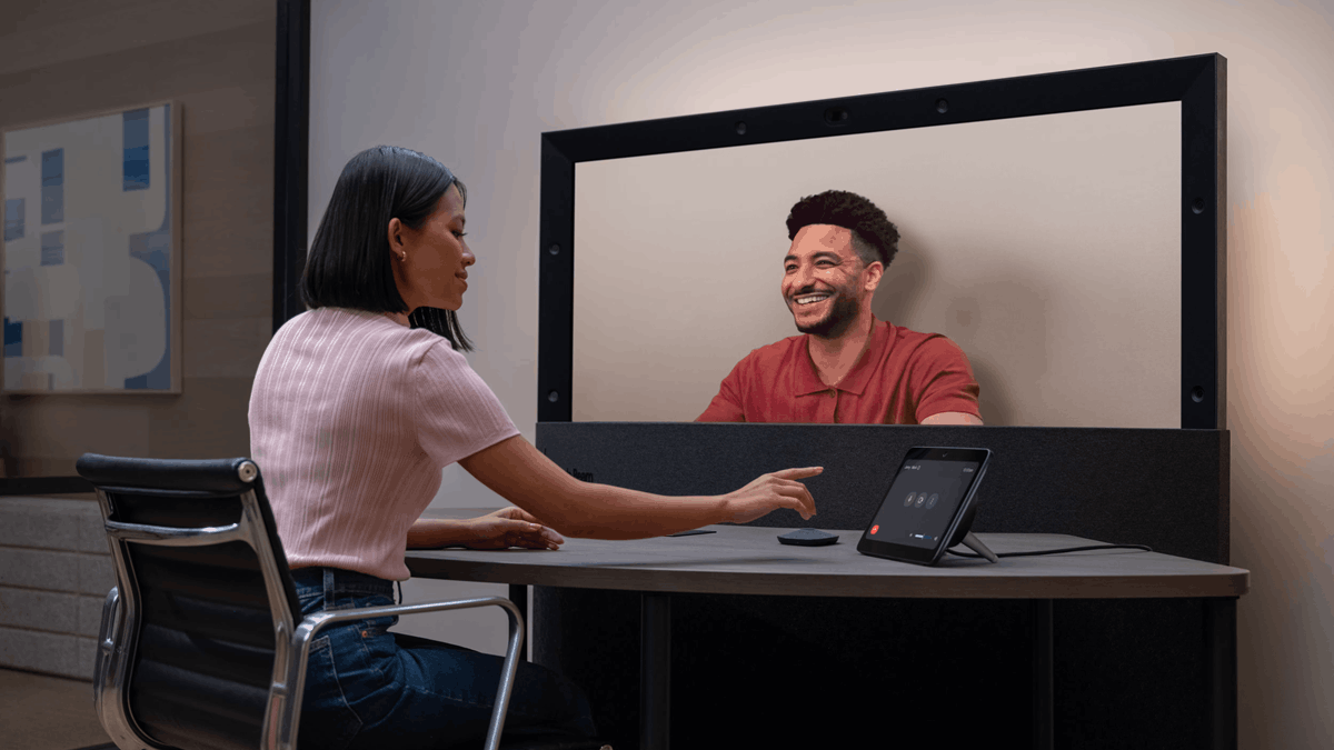 A woman interacting with a large 3D display showing a smiling man during a remote collaboration session