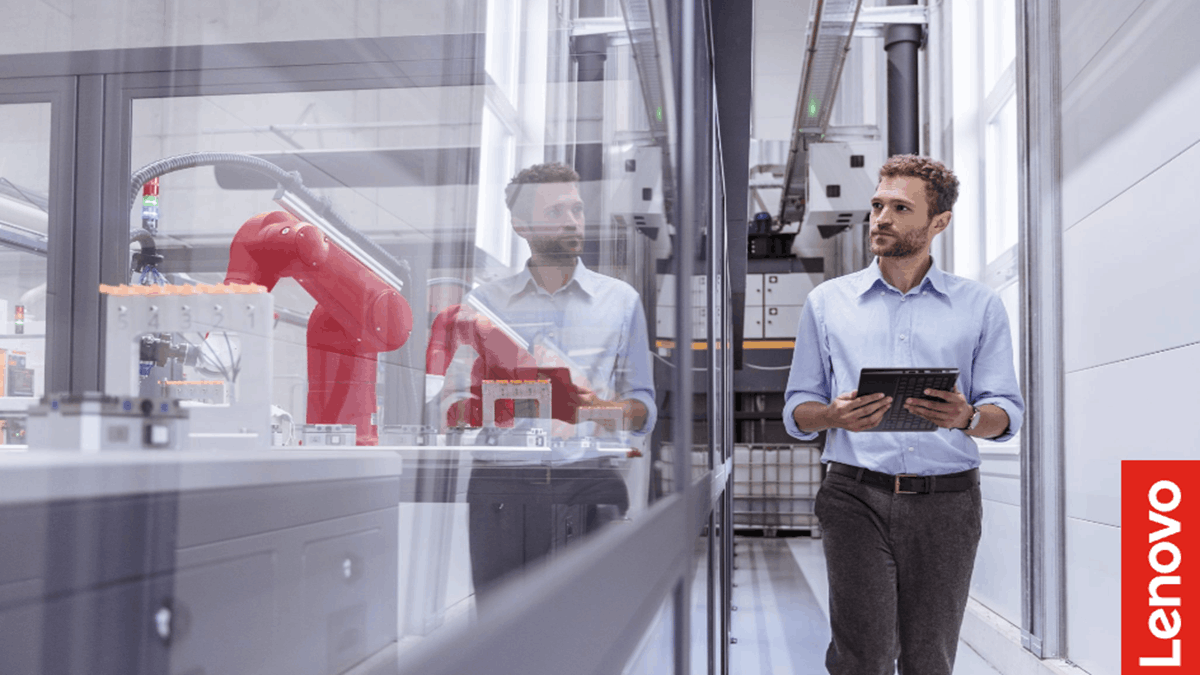 A professional walking through an automated industrial facility while monitoring operations on a tablet near robotic manufacturing equipment