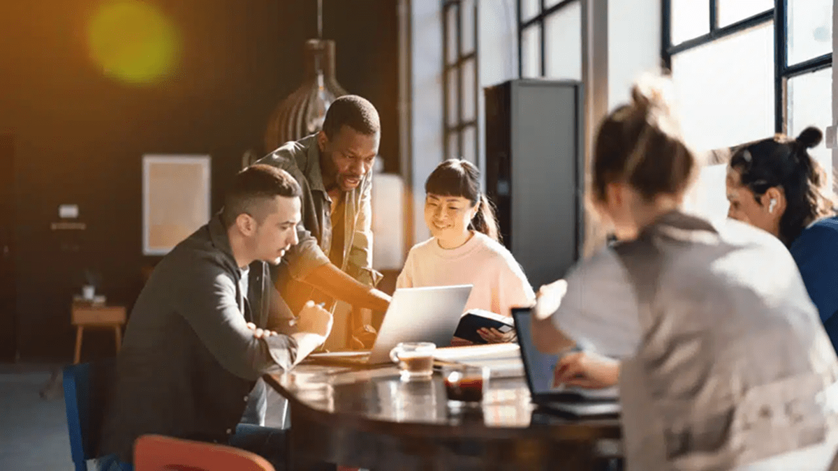 Group of professionals collaborating around a table with laptops in a sunlit modern office