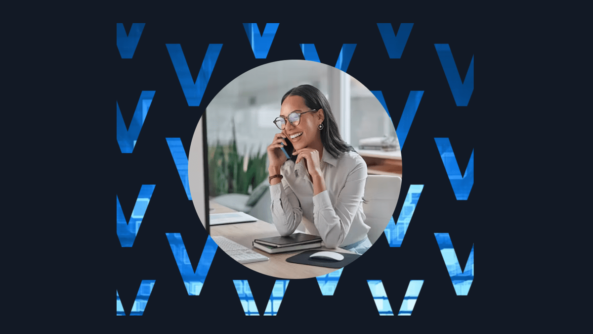 A professional woman smiling while speaking on the phone at her desk, representing customer engagement trends highlighted in Verint’s State of Customer Experience 2025 report
